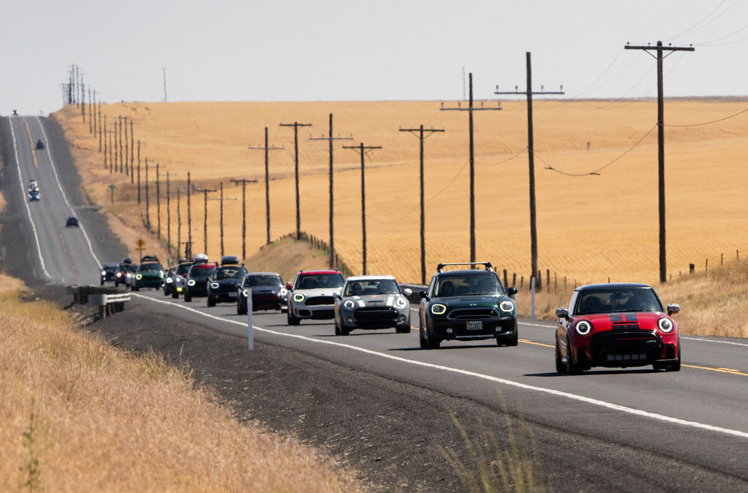 A convoy of MINIs on a two-lane road through wheat fields