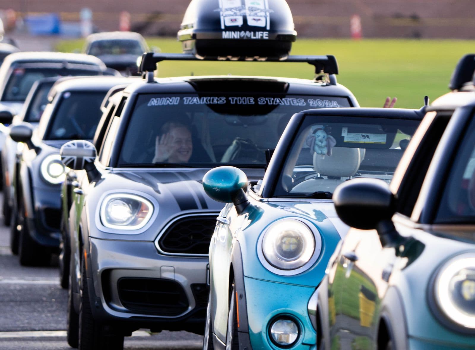 A driver waving from a MINI in a line of cars at a rally